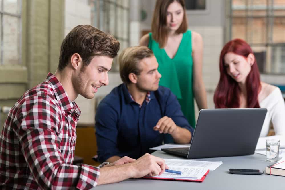 Group of Pretty and Handsome White Friends in Casual Clothing Busy Studying at the Worktable with Laptop Computer.