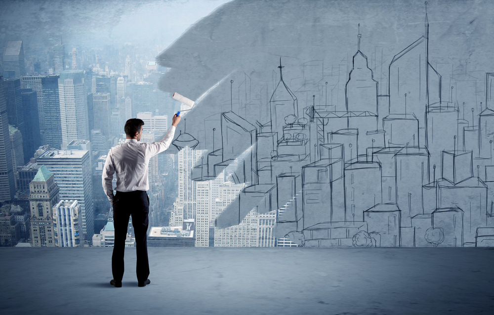 A businessman in elegant suit holding a paint roller in his hand and painting drawn city landscape over urban skyscrapers concept